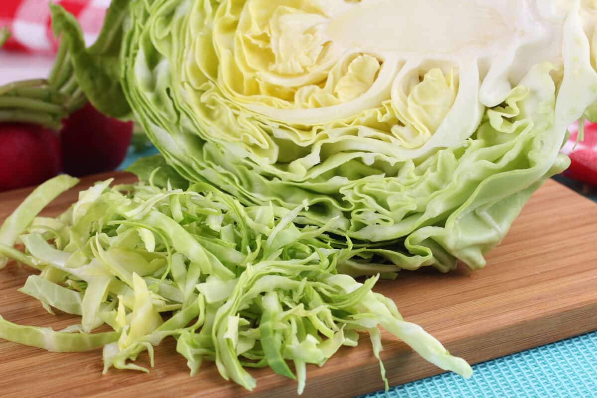 Sliced fresh green cabbage on a wooden cutting board.