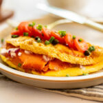 A smoked salmon omelet on a plate with a knife.