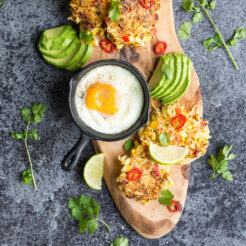 cropped image of spicy sweetcorn and potato fritters lay flat in the chopping board with sliced avocado and sunny side up egg