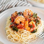 Spicy shrimp and kale served over angel hair pasta on a white plate.