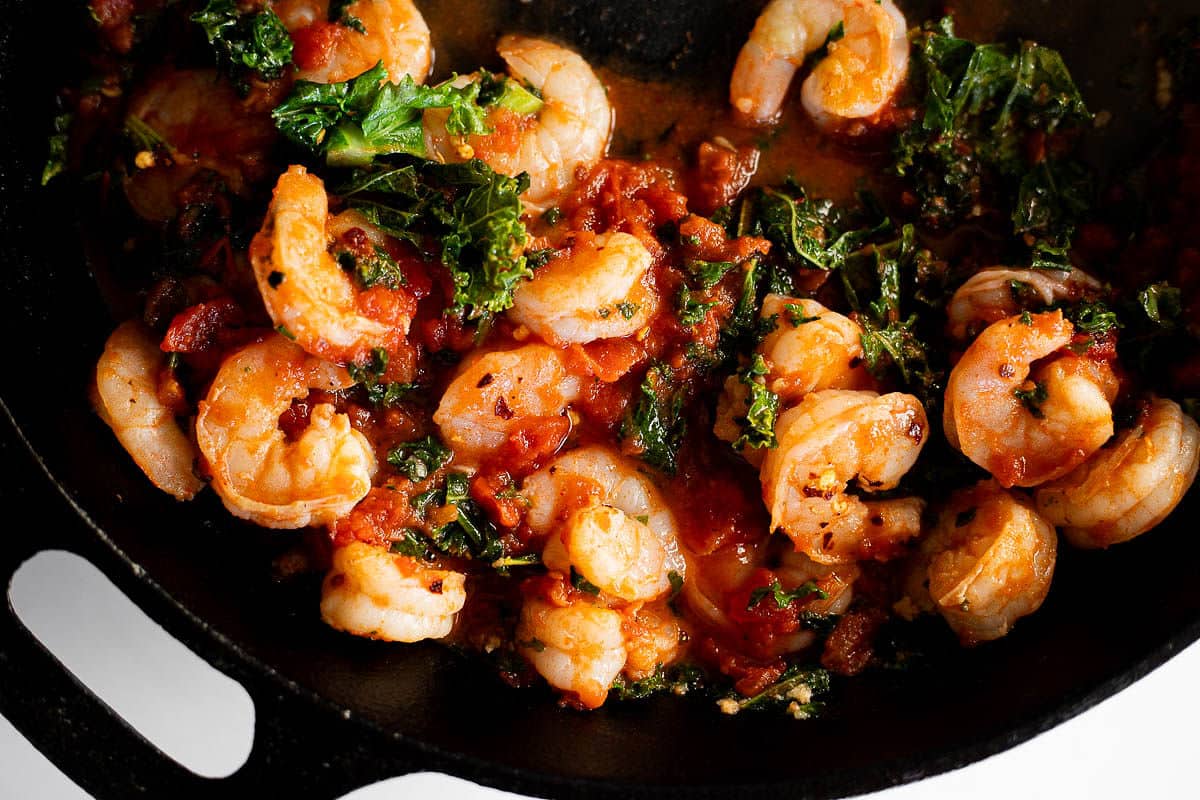 Spicy shrimp and kale with angel hair pasta in a cast iron skillet.