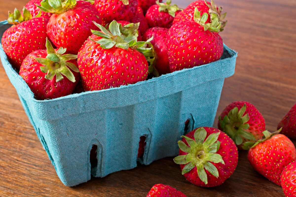 Close up quart of strawberries on a rustic wooden table. Part of the summer fresh fruit crop from the farmer's market.