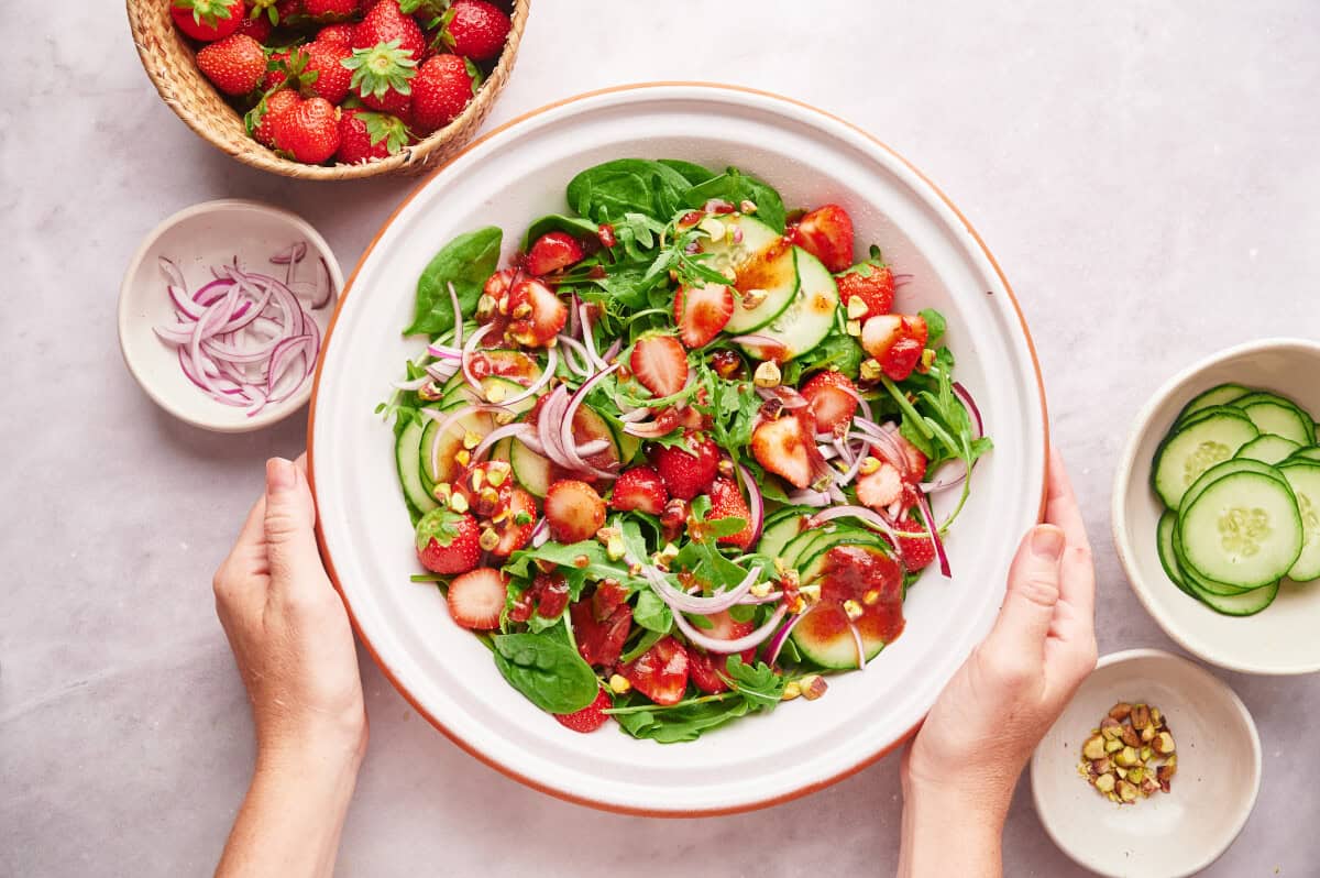 A woman's hands holding a large bowl of Strawberry Summer Salad with Strawberry Vinaigrette.