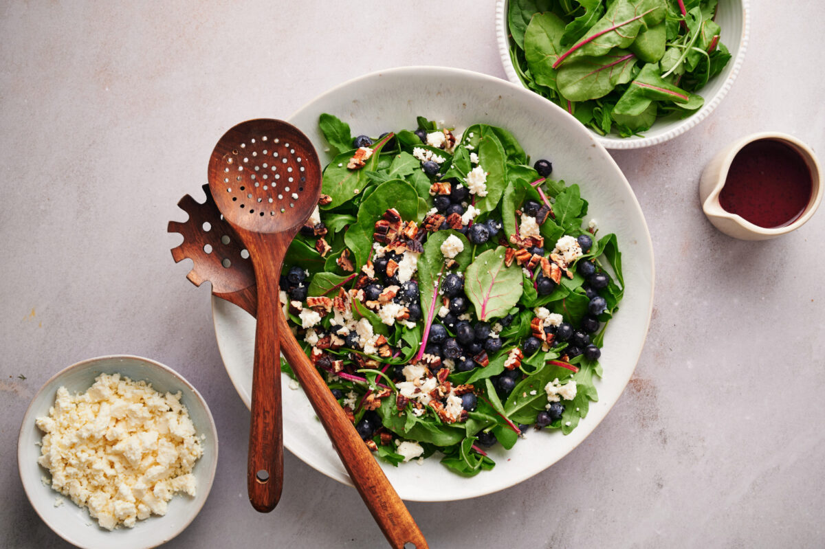 Spring mix (baby spinach and arugula) with blueberries, feta, and toasted pecans in a white bowl.