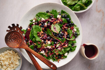 Top flat-lay view of summer blueberry salad with blueberries, feta, and toasted pecans in a white bowl with wooden utensils.