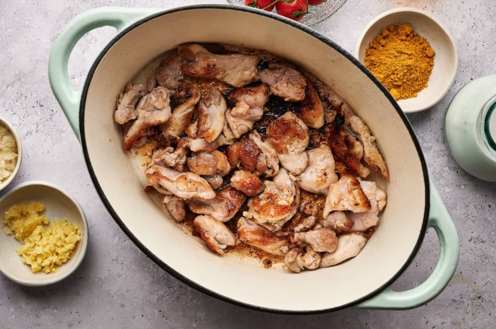 Chunks of chicken thighs browning in the bottom of a Dutch oven.