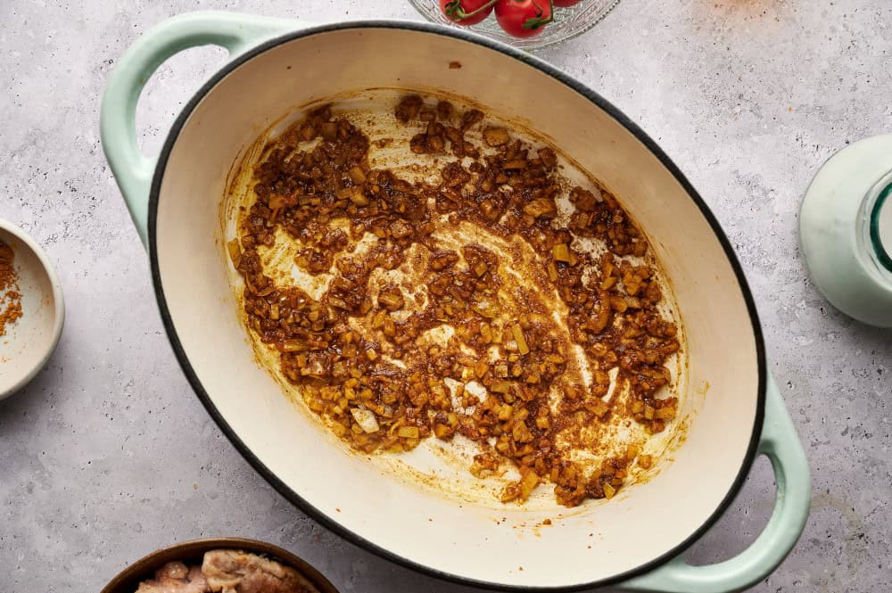 Sautéing onions, garlic, and curry in the bottom of a dutch oven to release aromatics.