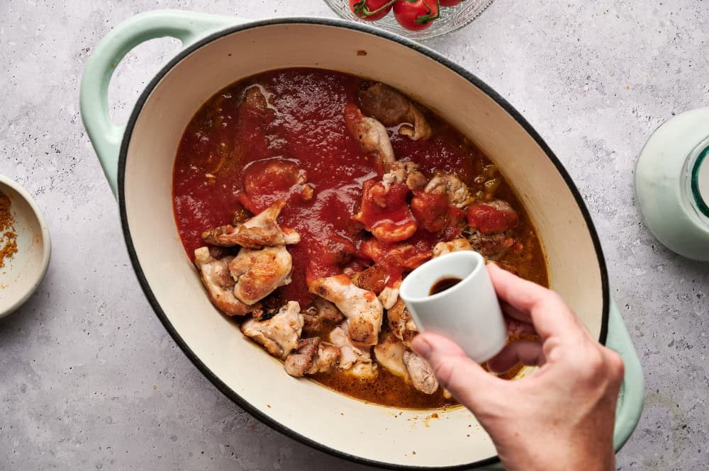 Pouring fish sauce into a Dutch oven filled with ingredients for Thai Chicken Coconut Curry.