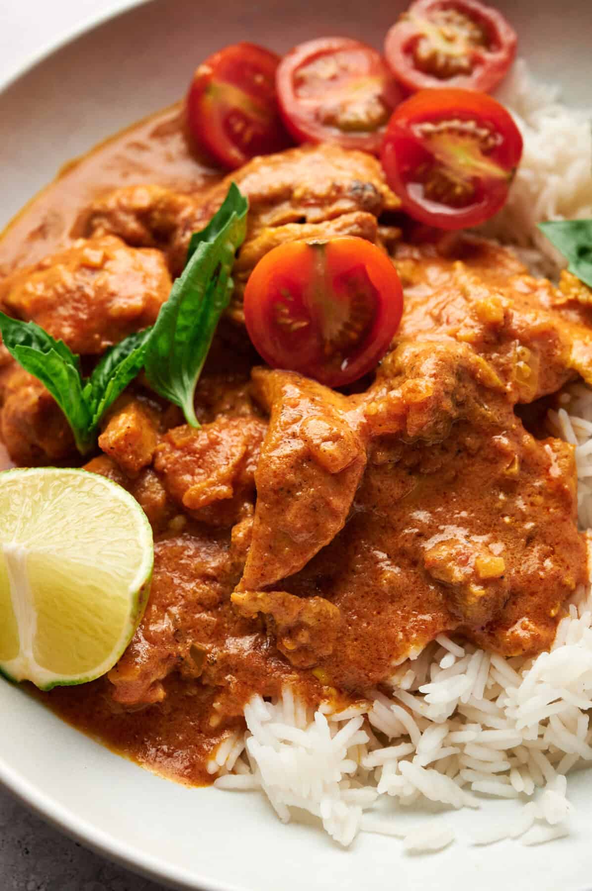 Close-up of Thai Chicken Coconut Curry garnished with lime, fresh tomatoes, and basil.