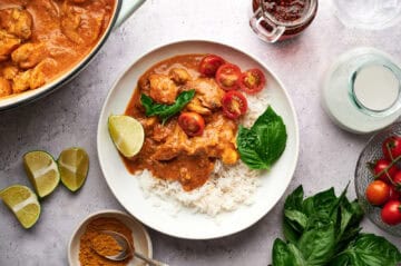 Thai Chicken Coconut Curry on a white plate, garnished with lime, fresh tomatoes, and basil.