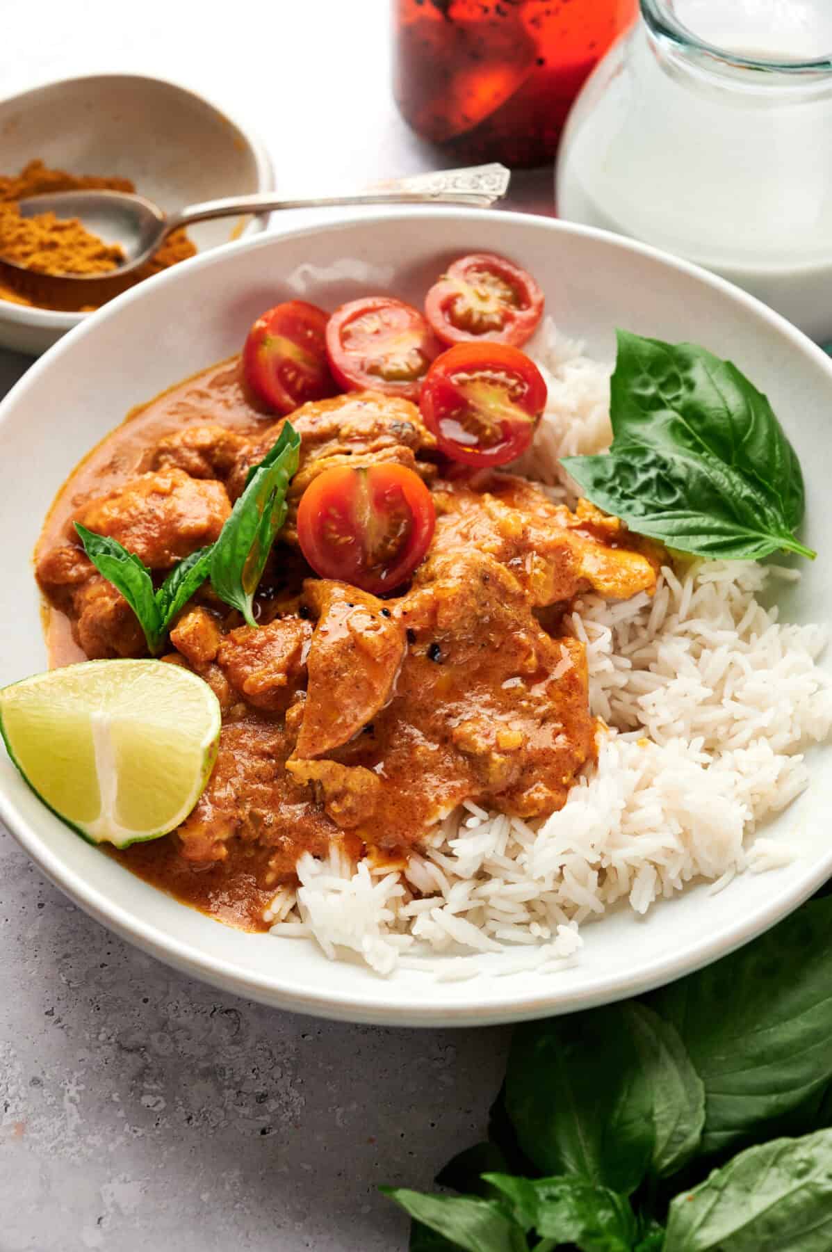 Vertically oriented photos of Thai Chicken Coconut Curry on a white plate, garnished with lime, fresh tomatoes, and basil.