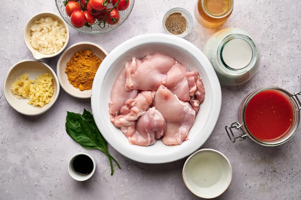 Ingredients for Thai Chicken Coconut Curry, with a bowl of raw chicken thighs featured in the center of the photo.