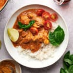 Thai Chicken Coconut Curry on a white plate, garnished with lime, fresh tomatoes, and basil.