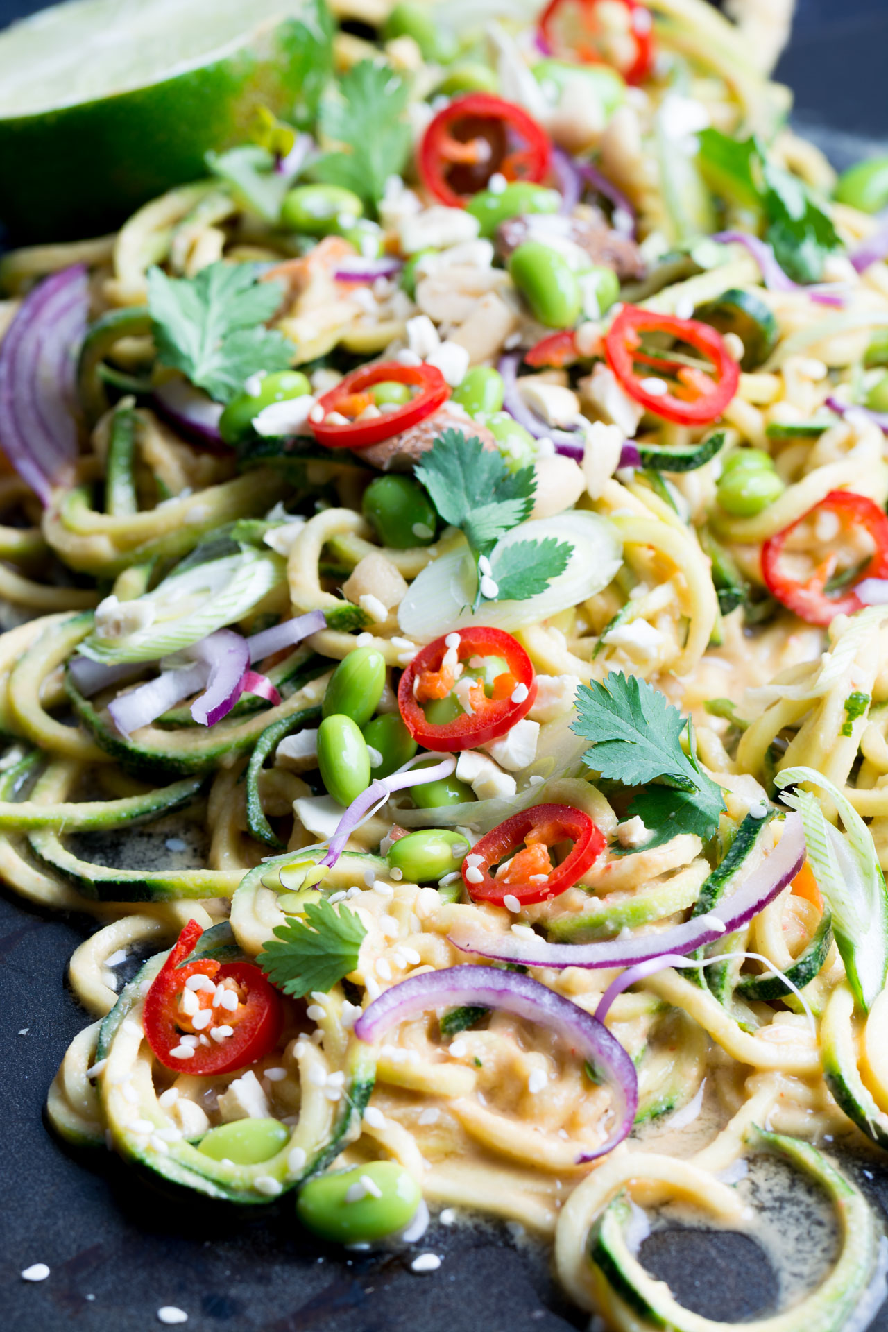 close up view image of a thai zucchini noodle salad top with edamame beans, onions, chopped red chili, peanuts, spring onions, parsley, and sesame seeds