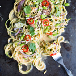 close up view image of a thai zucchini noodle salad top with edamame beans, onions, chopped red chili, peanuts, spring onions, parsley,