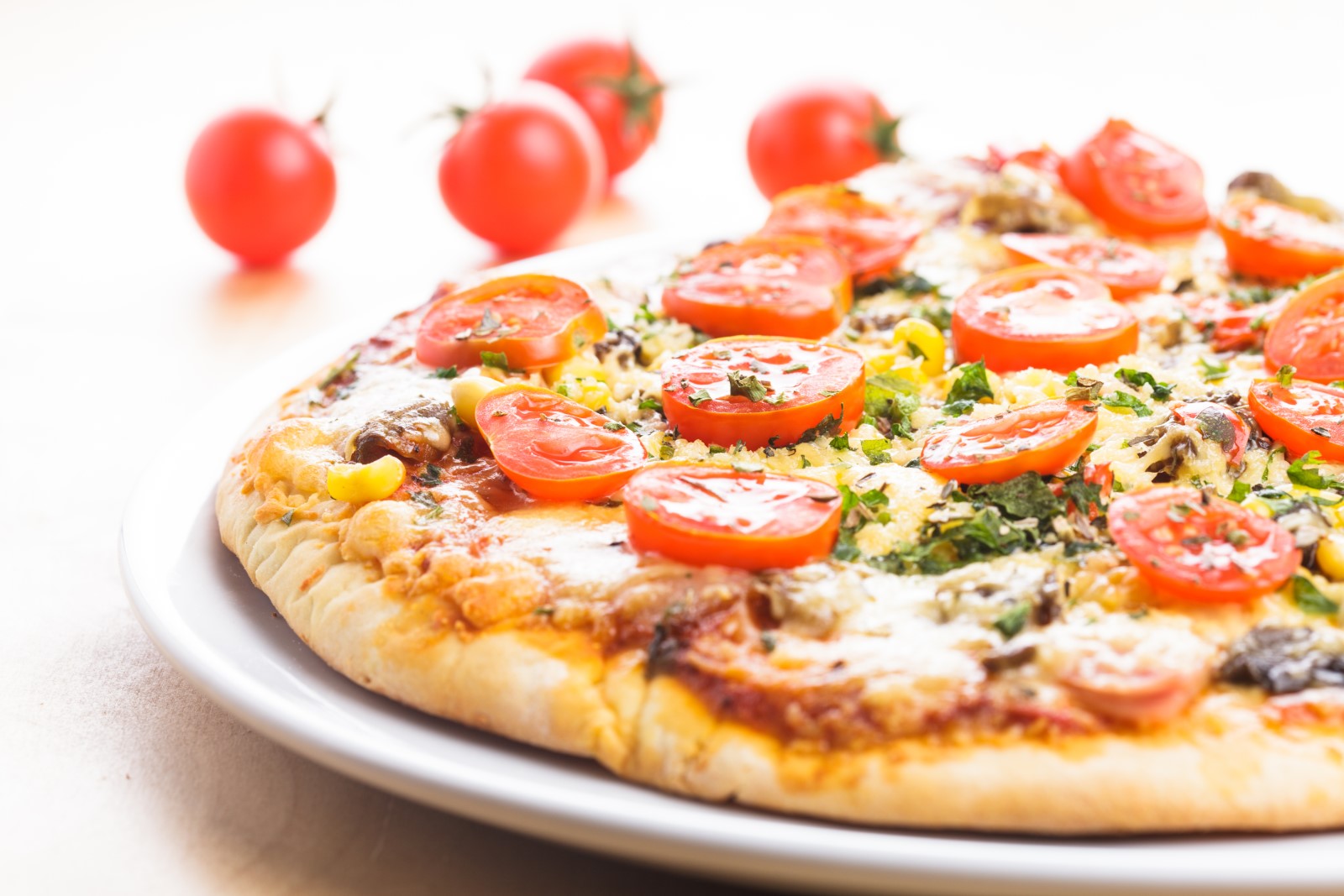 A whole pizza in a pizza pan topped with sliced tomatoes.