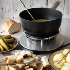 Slice of bread in a plate, a cooking pot and another plate with cheese cubes