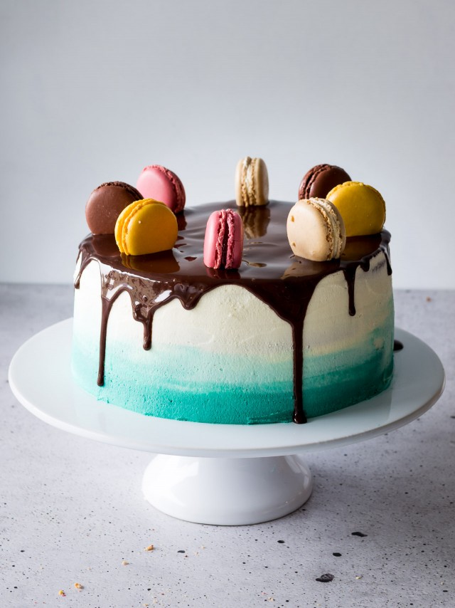 one whole vanilla ombre cake in a cake tray with colorful macarons on top