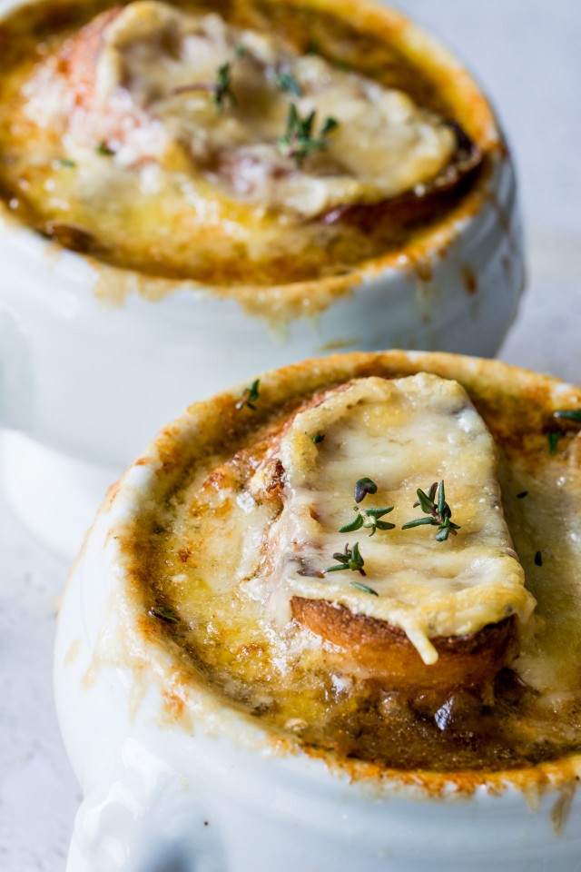 Close up of two bowls of Vegetarian French Onion soup topped with bread and cheese on a white table.