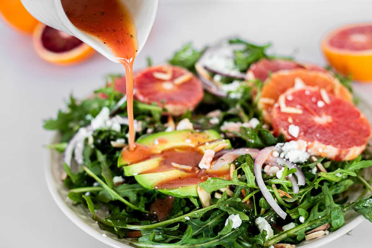 Pouring honey citrus vinaigrette over a winter citrus salad.