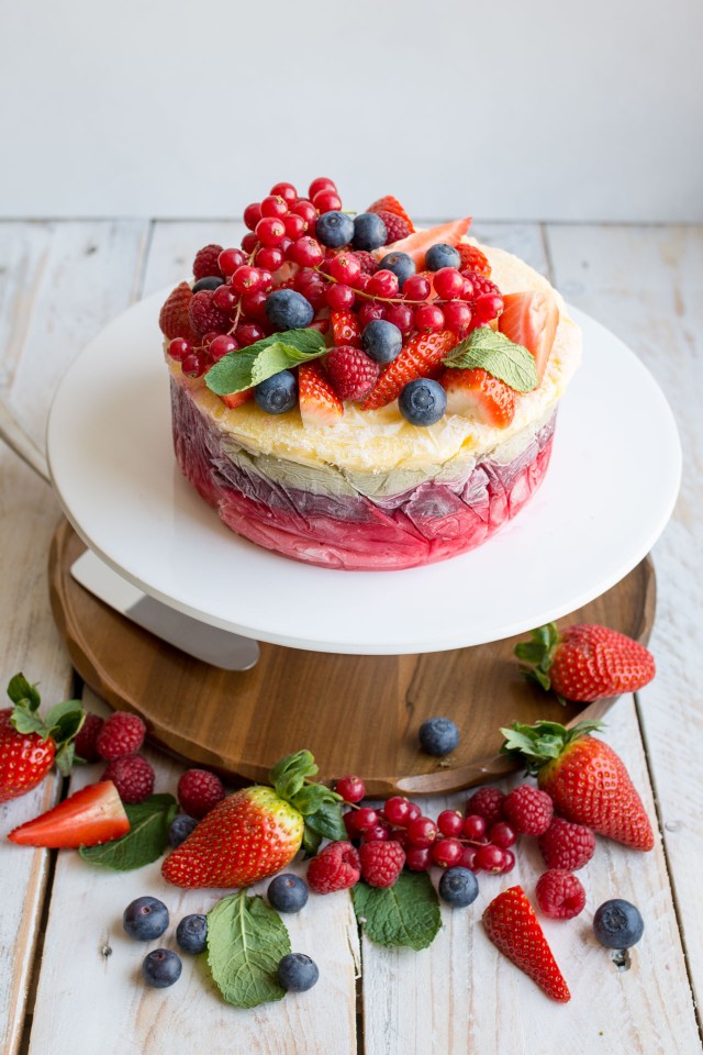 top down image of a delicious and colorful yogurt layer cake in a pedestal topped with strawberries, rapsberries, and blueberries